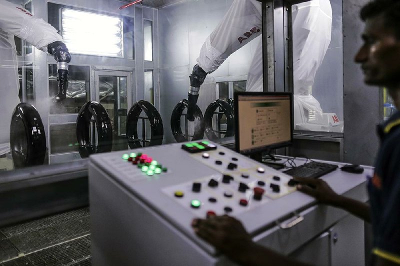 An employee stands at the control station as robotic arms spray lacquer onto mud guards for the Royal Enfield Motors Ltd. Classic 350 motorcycle at the company’s factory in southern India.