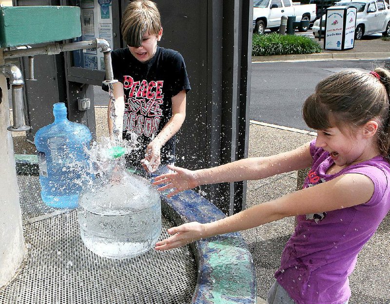 Greta Henning, 12, (left) and her sister Maggie Henning, 9, of Malvern react as water splashes from a jug fountain at Hill Wheatley Plaza in Hot Springs in May. Federal law requires Hot Springs National Park to provide spring water to visitors for free, park spokesman Mike Kusch said. 