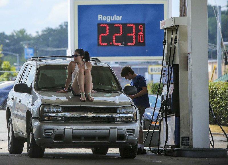 Jessica Troutman sits on the hood her friend Dalton Butler’s vehicle as he pumps gas Monday at an Exxon station on University Avenue. The average price of gasoline in Arkansas was $2.34 a gallon on Monday, down from $2.47 a month ago.