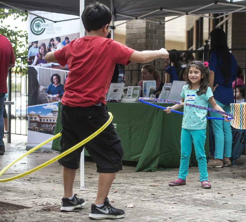 Sofia Ramirez, 5, watches Tuesday as her brother, Fernando, 9, tries a Hula Hoop during a block party and ribbon cutting for the Immigrant Resource Center in Springdale. The center is the first of five planned for the state.