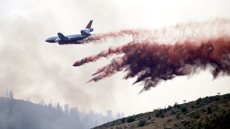 A tanker drops a load of fire retardant along a smoldering hillside Thursday in Twisp, Wash., a day after three firefighters were killed fighting a wildfire near the town. 