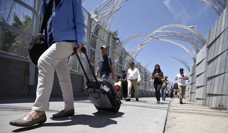 In this Aug. 18, 2015, photo, pedestrians pull suit cases and newly bought goods as they trek up the new pedestrian walk way to the Mexico border crossing in San Ysidro, Calif.