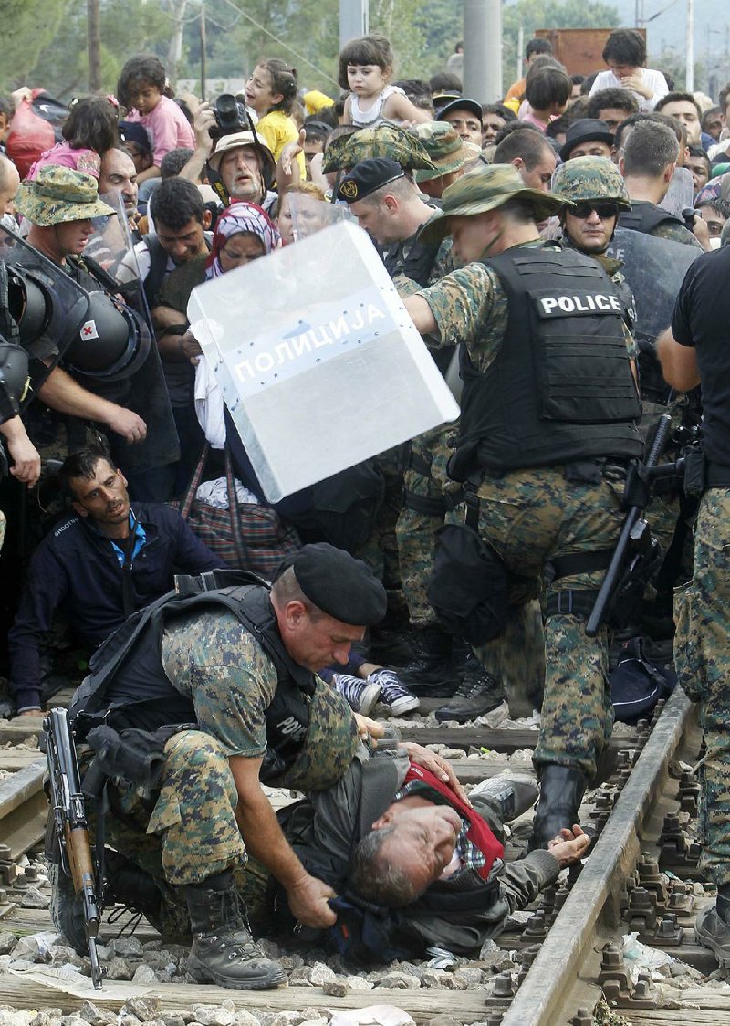 A Macedonian police officer helps a man who collapsed while migrants and police faced off Friday as the crowd tried to enter Macedonia at the border with Greece. 