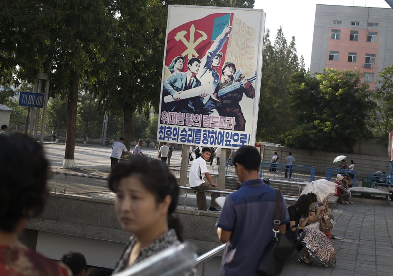 A man sits under a propaganda banner in Pyongyang, North Korea, Sunday, Aug. 23, 2015. North and South Korea on Sunday resumed a second round of talks that temporarily pushed aside vows of imminent war on the peninsula. (AP Photo/Dita Alangkara)