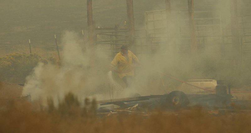 A firefighter sprays burning debris Wednesday next to a mobile home near Omak, Wash., keeping the flames from reaching the home.