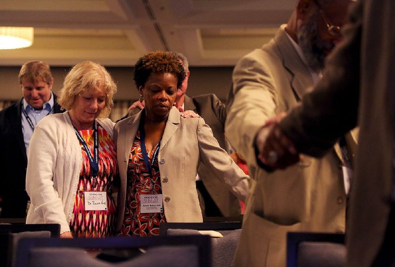 Debra Hurd (left) and Annette Thomas-Jones embrace Wednesday as others join hands during the closing prayer of the Governor’s Restore Hope Summit in Little Rock. State officials asked the leaders of churches and other faith-based organizations to help create opportunities for foster children and also for inmates who are transitioning back into society.