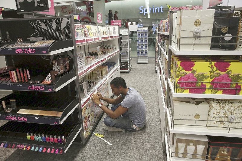 An employee puts final touches Wednesday on a shelf display in the makeup section of the Macy’s Backstage store in New York City.