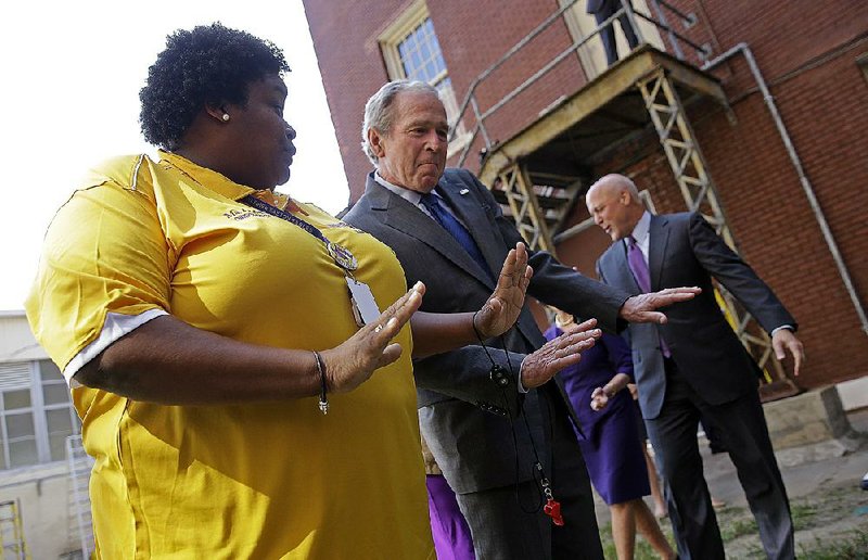 Former President George W. Bush shows off some moves with band director Asia Muhaimin as the Warren Easton Charter High School band plays during Bush’s visit Friday to New Orleans. Behind are former first lady Laura Bush with New Orleans Mayor Mitch Landrieu.