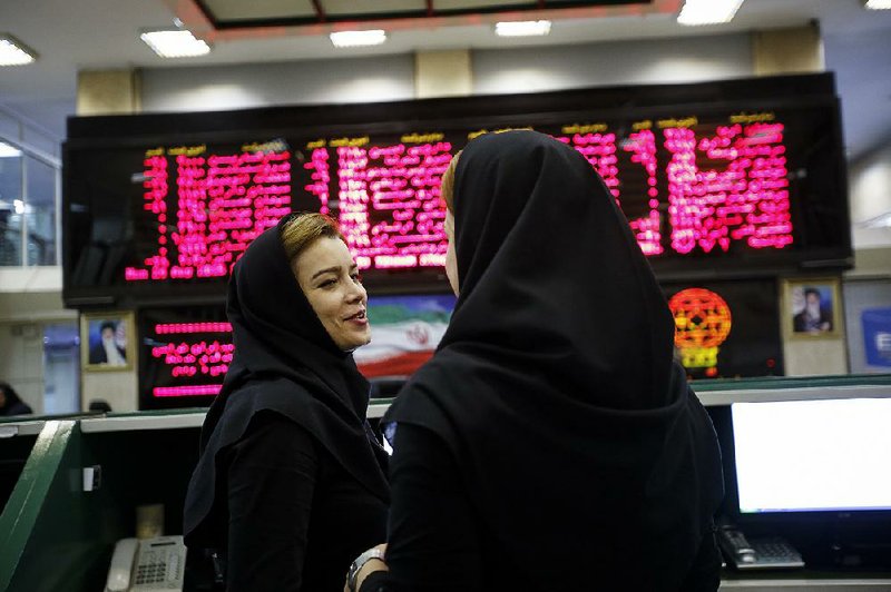 Female employees talk beneath electronic screens displaying financial data at the Tehran Stock Exchange in Tehran, Iran, on Aug. 24.