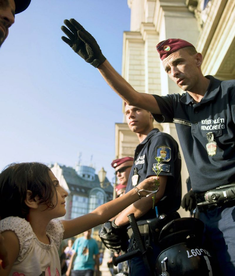 A migrant girl offers a flower to a police officer during a demonstration Tuesday outside a closed railway station in Budapest, Hungary, after migrants were not allowed to board trains bound for Germany because authorities say they don’t have valid documents.