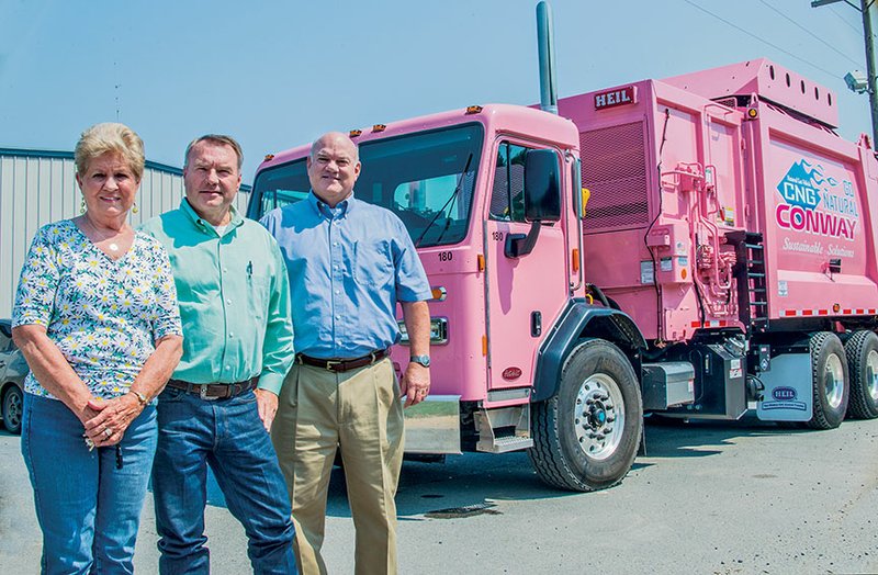 Jean Jasso, from left, and Ross Harrington, mother and husband of the late Cheryl Harrington, who was the Conway sanitation director, and Jack Bell, interim director of the department, stand next to the residential truck that was painted pink to honor Harrington’s memory. She died in March of cancer. Three other pink trucks were ordered and will bear her name. There was no additional cost for the pink paint, Mayor Tab Townsell said. The sanitation complex and street into the area were named after Harrington, too.