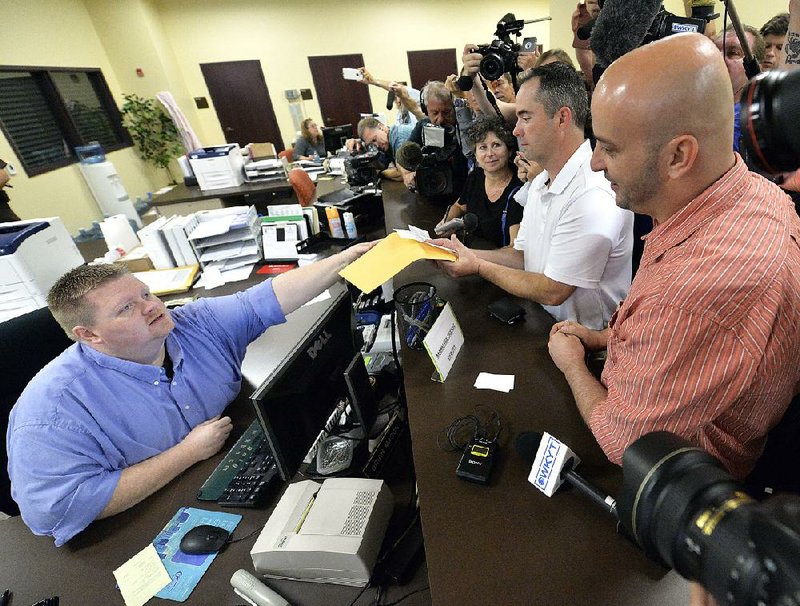 Brian Mason (left), a Rowan County, Ky., deputy clerk, hands a marriage license Friday to James Yates and his partner, William Smith Jr. (right), at the county clerk’s offices in Morehead, Ky. Yates and Smith said they had made several attempts to get the license.