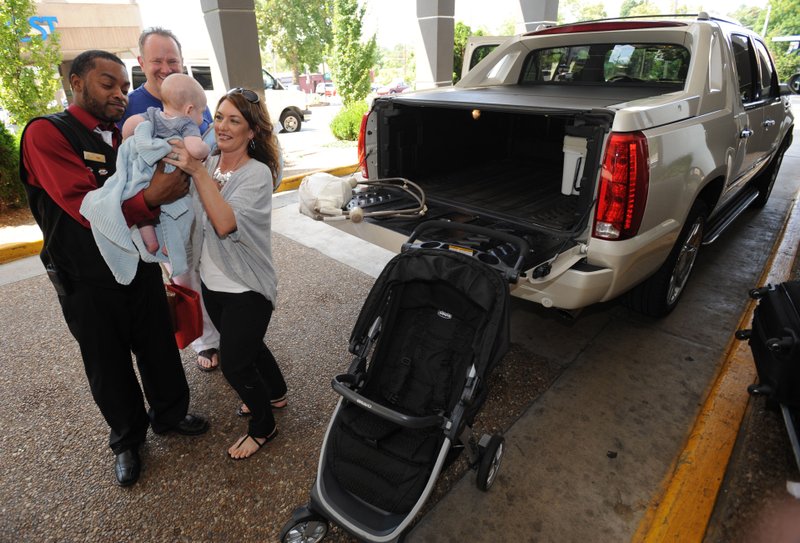 Mitch Collins (top) and Stacy Prout (right) of Conway smile Friday as Tony Blackburn, bell and valet manager for The Chancellor Hotel, returns their 4-month-old son, Colt Collins, while helping them load their belongings into the hotel ahead of today’s Razorbacks season-opening football game in Fayetteville. The couple have become very close friends with Blackburn after coming to the hotel for games over the years and enjoyed catching up as they moved into their room.