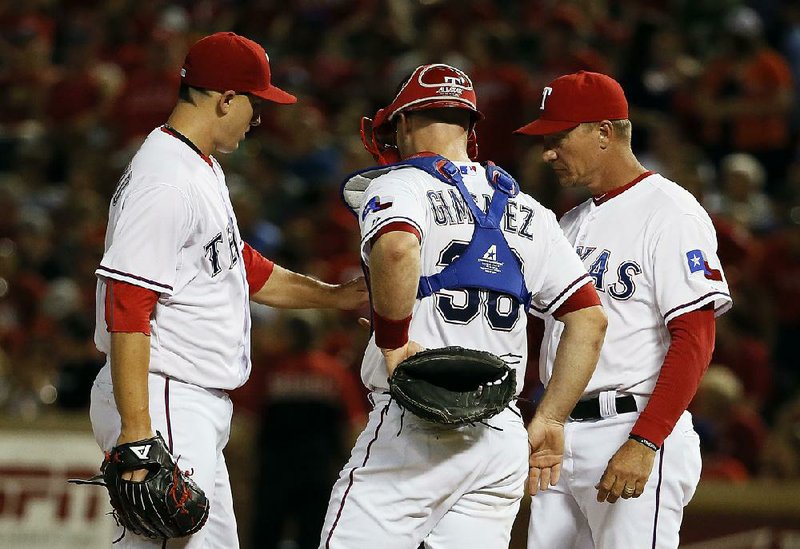 Texas starter Derek Holland (left) hands the ball to Manager Jeff Bannister as catcher Chris Gimenez watches during the Rangers’ 6-5 victory over the Houston Astros on Tuesday in Arlington, Texas. Holland allowed all 5 Astros runs on 10 hits with 2 walks and 1 strikeout in 5 2/3 innings pitched.