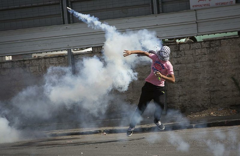 A Palestinian throws back a tear gas canister at Israeli soldiers Tuesday after a demonstration in the West Bank town of al-Ram, held in solidarity with protesters at the Al-Aqsa mosque compound in Jerusalem’s Old City. 