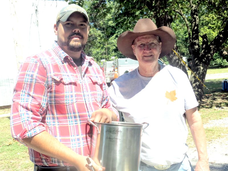 Anthony Bertschy, left, of Hiwasse, won the $50 prize when his pot of chili was voted the tasters’ favorite in the contest at the Hiwasse fall festival Saturday. He added his name to the chili pot just below that of Larry Weihe, right, reigning chili champion as winner of the 2014 chili cooking contest.