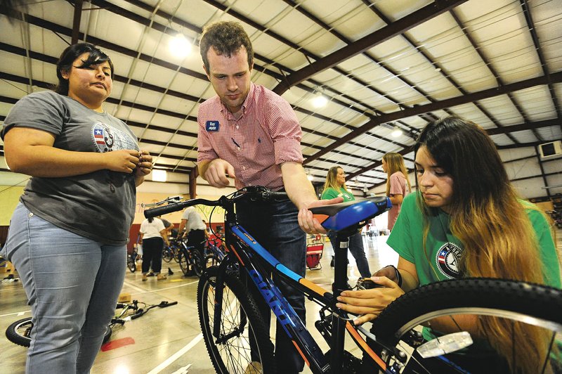Daniela Alvarado (left) and Denise Bravo (right), both Americorps volunteers, work with Ray Ford (center) of Arvest Bank as they assemble a bicycle Friday at John Tyson Elementary School in Springdale. Volunteers assembled the last 32 of a total 850 bicycles funded by a grant to Springdale Public Schools from the Walton Family Foundation.