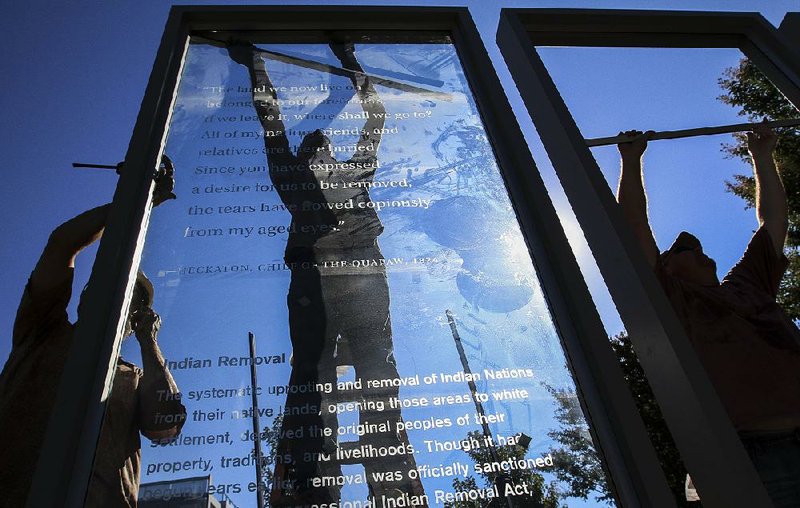 Arkansas Democrat-Gazette/BENJAMIN KRAIN --09/17/15--
From left, David Soos, Nathan Cathey and Ronnie Dworshak install one of five glass panels in front of the Clinton Library with quotes and information from several historical civil-rights events in Arkansas such as the slave trade, the Trail of Tears,  Japansese internment camps and the desegragation crisis of 1957. The panels will be part of a permanent installation circling a chute from Anne Frank's tree. The sapling will be planted during a special ceremony Oct. 2. 