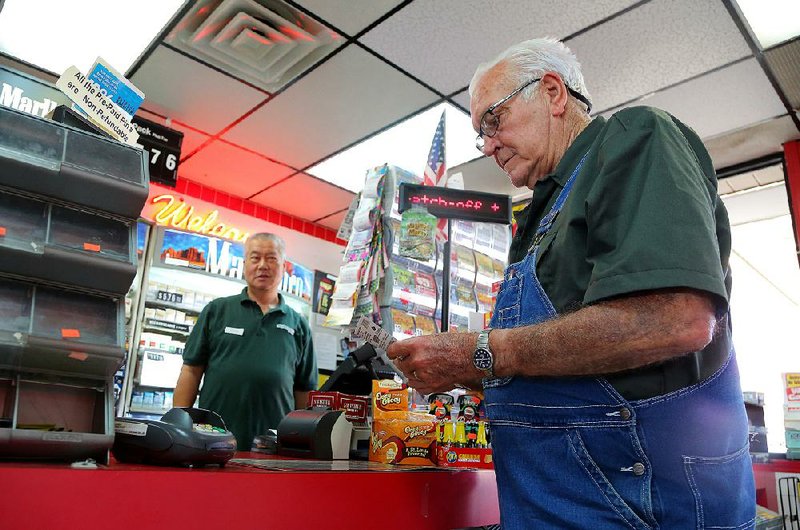 Eddie Park (left), owner of the Y&E Superstop in Bryant, watches as regular lottery customer Roger Urrey of Bryant checks his tickets Thursday. The convenience store racked up $1.89 million in lottery sales in fiscal 2015, or about $5,178 per day. 