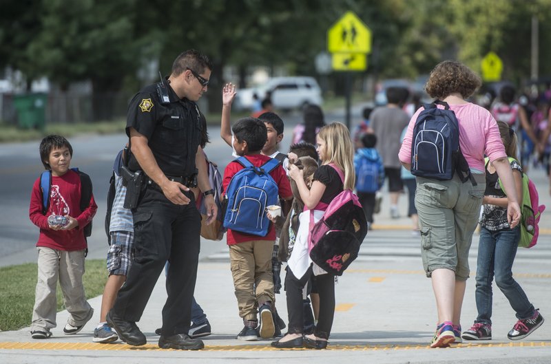 Eric Cardenas, school resource officer, greets children Thursday at Jones Elementary School in Springdale. Cardenas talks with the children and helps keep traffic steady, smooth and safe for the children. Overall crime rates are down or stable in Northwest Arkansas.