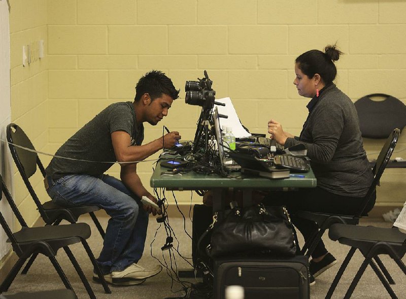 Elmer Beltran signs a signature pad as he gets a passport Friday from Guatemalan Consulate staff member Maria Esparza at a mobile site in Little Rock.