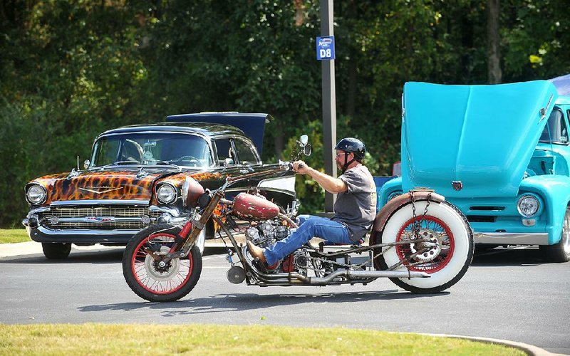 Darrel Buford of Pryor, Okla., rides his custom-built rat bike past cars at the Car/Truck Show on Friday at Arvest Ballpark in Springdale. The car show continues today as part of the 16th annual Bikes, Blues and BBQ motorcycle rally, which is hosting events in Northwest Arkansas.
