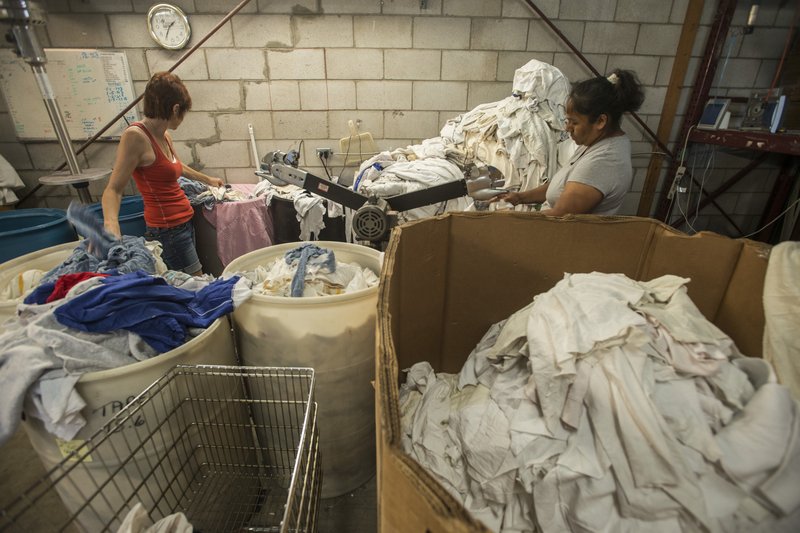 Vivian Nichols, left, and Norma Perez, both with Northwest Rags, Inc., cut torn pieces of rags apart Wednesday to salvage the rags at the company’s facility in Springdale. Vance Brock, owner of Northwest Rags, ships used clothing all over the world, and has a line of industrial rags, Ozark Recycled Wiping Rags. For more photos, go to www.nwadg.com/photos. 