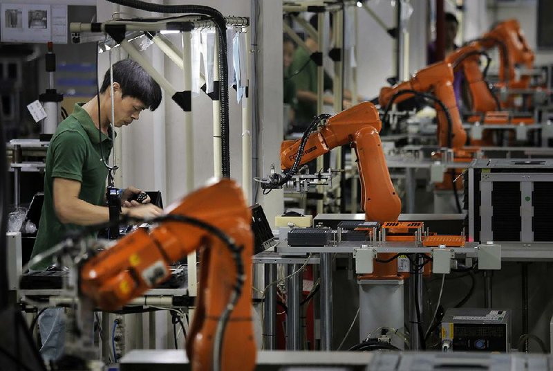 A worker stands on the line alongside orange robot arms at the Rapoo Technology factory in the industrial town of Shenzhen in southern China.