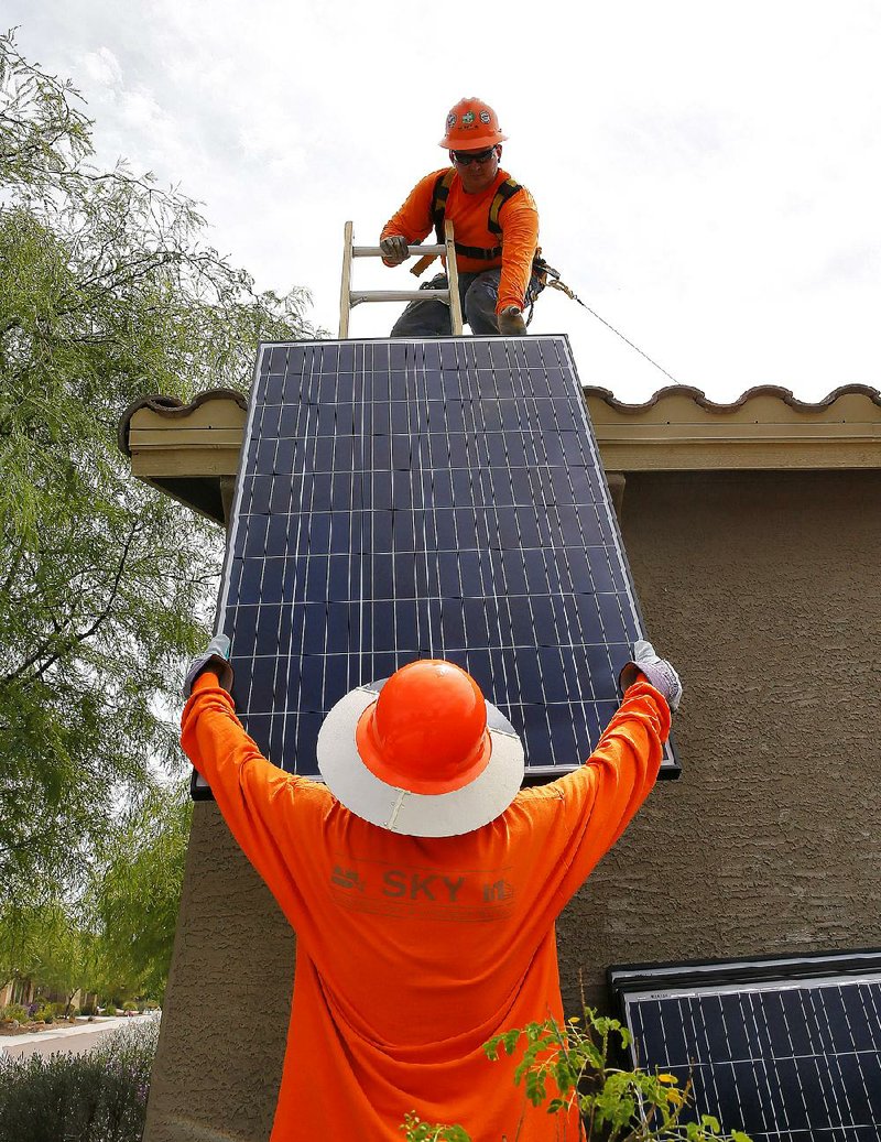 Electricians install solar panels on a roof for the Arizona Public Service Co. in Goodyear, Ariz., in July. 
