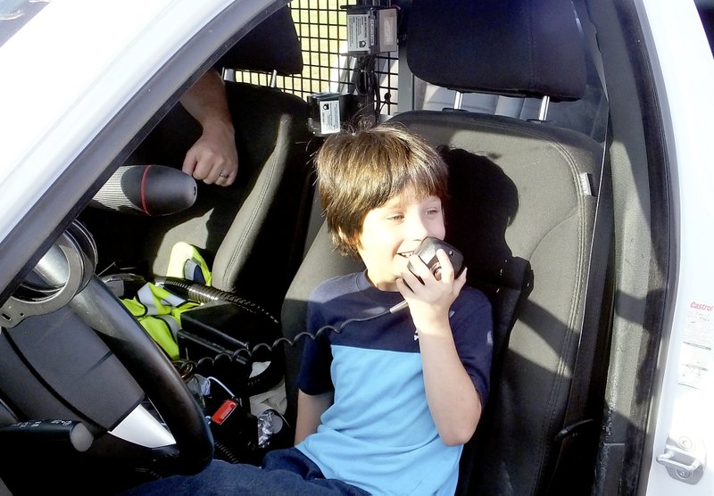 Lynn Atkins/The Weekly Vista Kindergartner Dakota Keymer gets a chance to use the microphone in a Bella Vista police car at Careers on Wheels Day at Cooper Elementary School. The school counselors invited people who use vehicles in their work to show them off at the school.