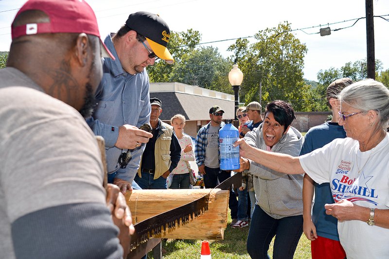 Tony Thomas, front, and his wife, Danielle, center, saw a log at last year’s Crosscut Saw competition at the Ozark Trail Festival. Bonnie Sherrill, right, lubricates the saw and wood while Josh Barger of Quitman sits on the log to ensure its stability.
