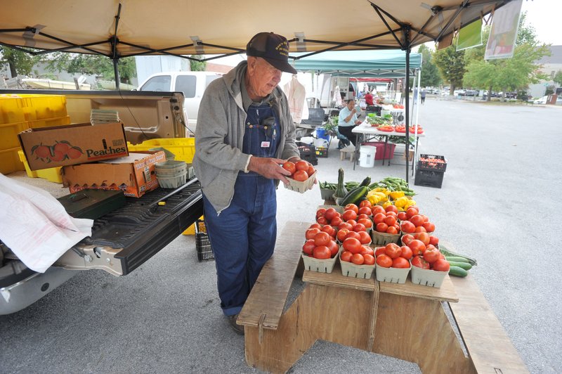 John Obenshain, a Rogers Farmers Market producer for more than 15 years, sets out a basket of fresh tomatoes Wednesday morning at the farmers market in Rogers. Obenshain is one of several longtime vendors at the market who weren’t happy to hear the announcement Main Street Rogers will take over ownership of the market starting next year.