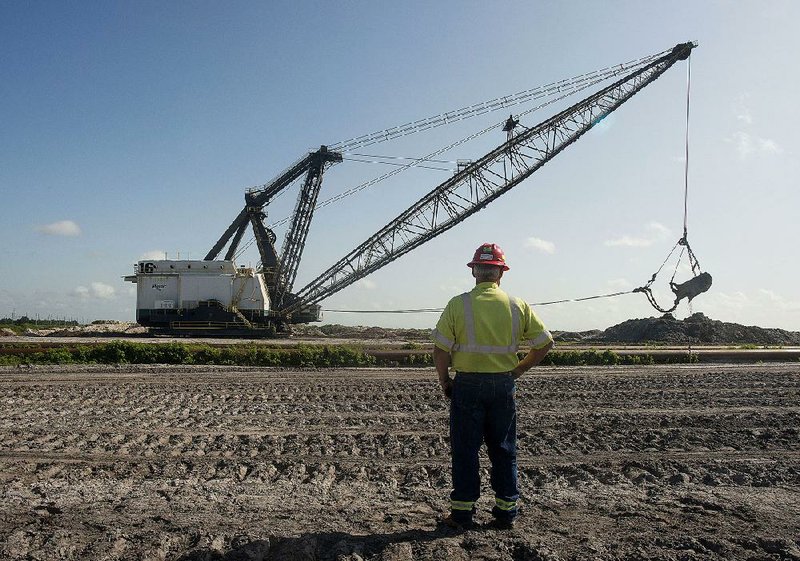 An employee watches as the bucket of a drag line unearths phosphate in July at the Mosaic Co. South Fort Meade phosphate mine in Fort Meade, Fla.