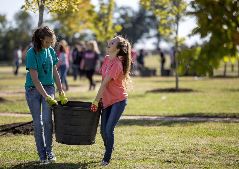 Bentonville High students Ally Sperry (left) and Emily Young carry a bucket of mulch Thursday at Orchards Park in Bentonville. Students and teachers teamed up with the Parks and Recreation Department to beautify Orchards Park in the first Civics Community Involvement Day.