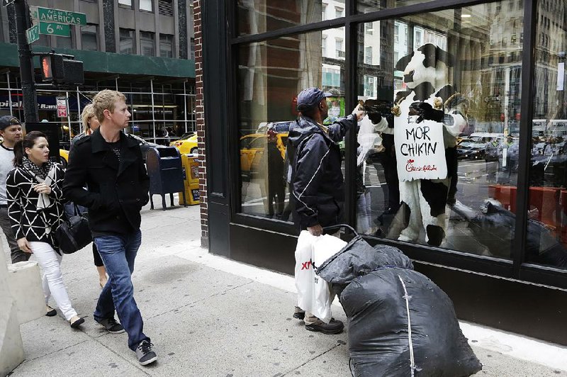 People pass a Chick-fil-A “cow” in the window of a new Chick-fi l-A restaurant in New York City that opens today.