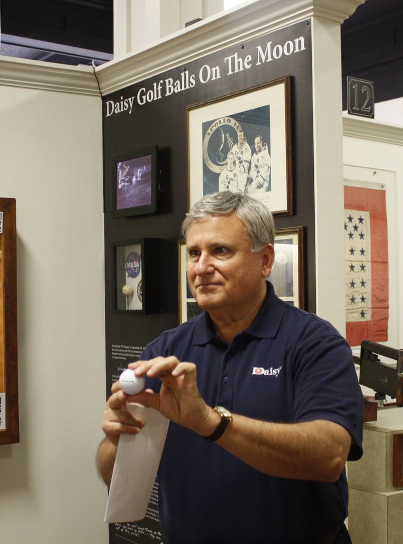 Joe Murfin, chairman of the board of directors at Daisy Air Gun Museum, holds a golf ball up Monday while standing in front of a new display about two golf balls that bear the Daisy logo that are on the moon.