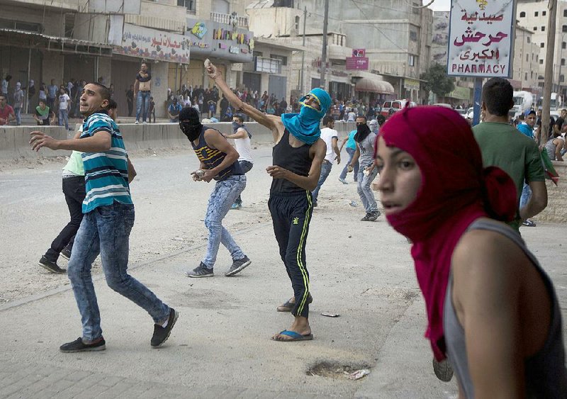Young Palestinians hurl stones at Israeli forces Tuesday at the Qalandia checkpoint between Jerusalem and the West Bank city of Ramallah. With a recent rise in violence, Israeli Prime Minister Benjamin Netanyahu has threatened to take “strong action.” 