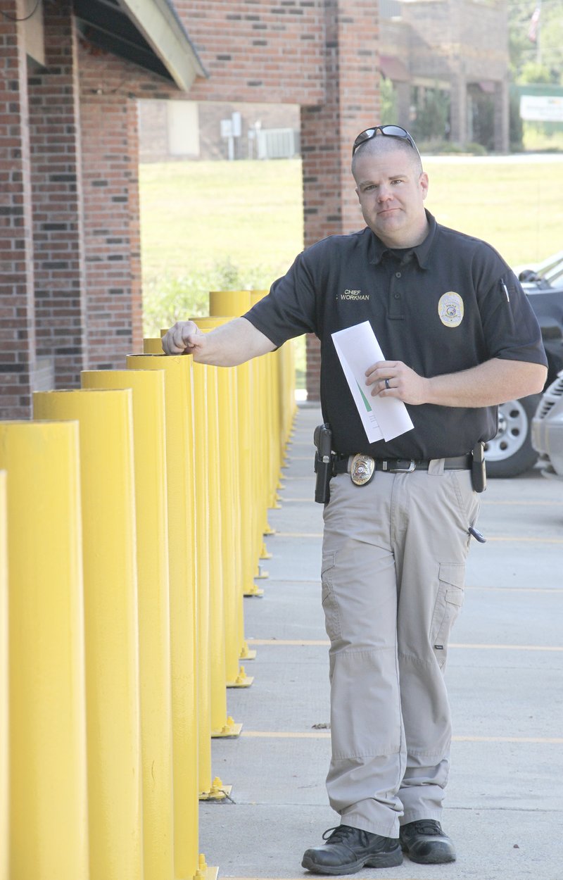 LYNN KUTTER ENTERPRISE-LEADER Chris Workman, Prairie Grove police chief, shows off yellow bollards placed in front of the district court and police station to stop vehicles from driving into the building. Caps had not been placed on top of the bollards in this photo.