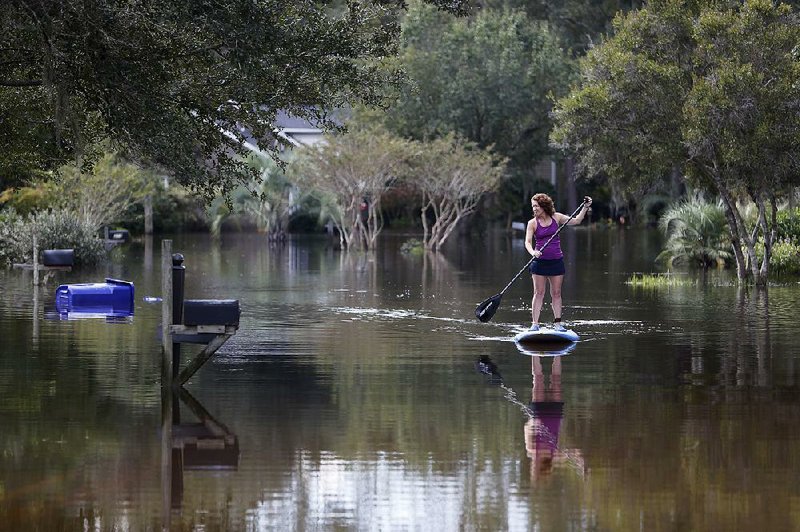 Tara Saracina travels her street by paddleboard Thursday in Summerville, S.C., northwest of Charleston. As water from recent fl ooding continues to fl ow toward coastal areas, a canal that provides a main source of drinking water for Columbia, S.C., collapsed in two places. Contractors hurried to plug the holes Thursday, and National Guard helicopters dropped sandbags on the breaches.
