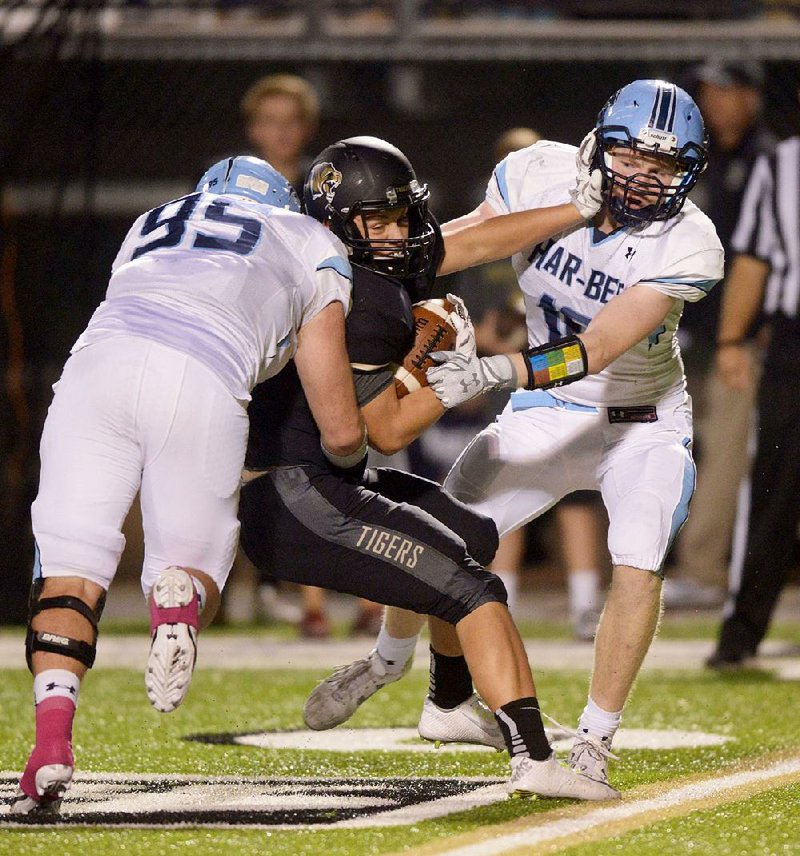 Springdale Har-Ber defenders David Vowell (left) and Chase Anderson (right) tackle Bentonville running back Jacob Clark during Friday night’s game. The Wildcats remained unbeaten in 7A-West play and ended the Tigers’ 14-game winning streak. 