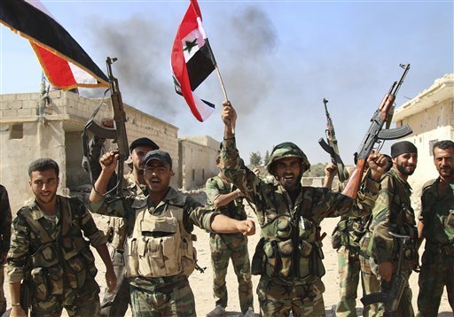 In this photo taken on Sunday, Oct. 11, 2015, Syrian soldiers waving Syrian flags celebrate the capture of Achan in Hama province, Syria.