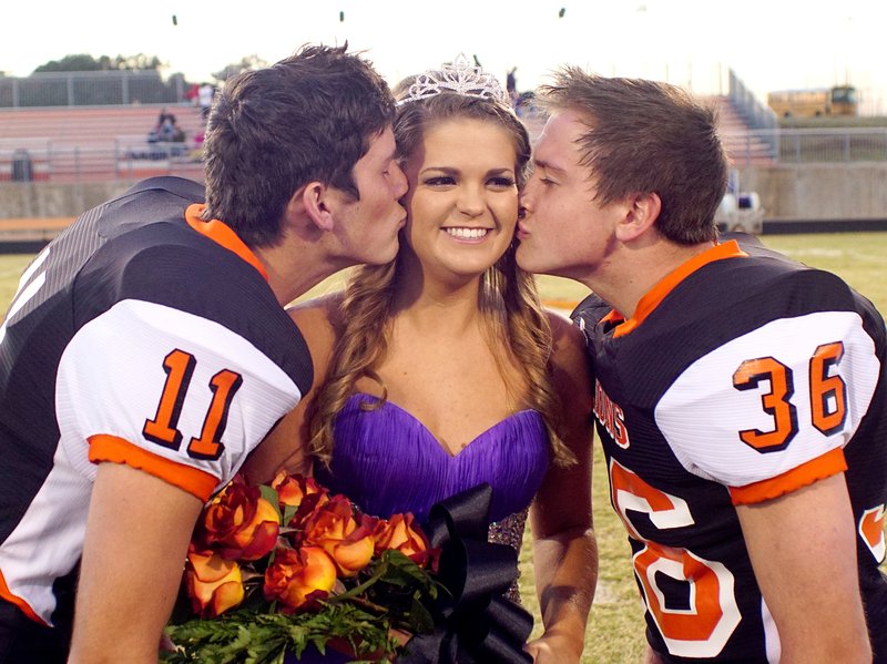 2015 homecoming queen, Kaitlyn Sands, is kissed by her escorts, Kilby Roberts and Jace Russ, during coronation ceremonies in Gravette on Friday.