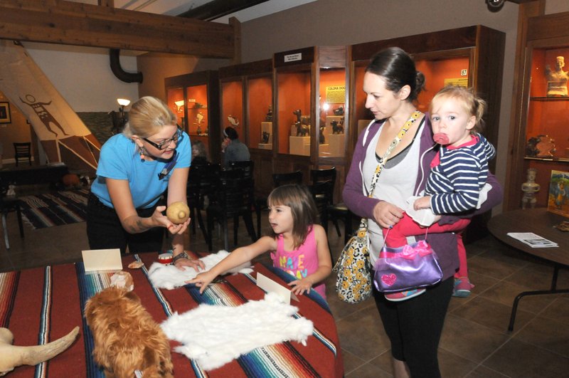 Sarah Benson (left) with the Museum of Native American History in Bentonville shows Friday some touchable items to Meagan Ruffing of Bentonville and her children Elinor (left) and Hannah. Benson read stories and led activities Friday during the museum’s story time. 