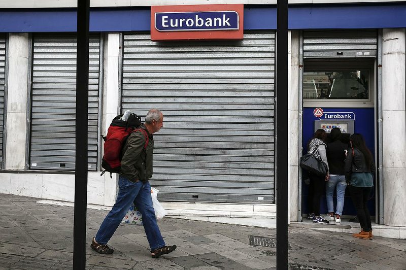 A tourist walks past as youths make a transaction at the ATM of a Eurobank branch Saturday in Athens, Greece. 