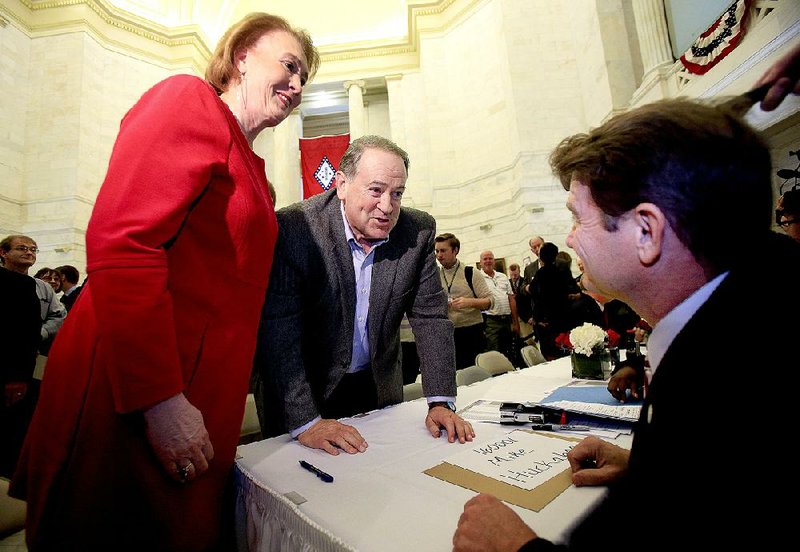 Former Arkansas Gov. Mike Huckabee (center), accompanied by his wife, Janet, on Monday talks with Secretary of State Mark Martin during the first day of filing for office at the state Capitol. Huckabee filed as a Republican candidate for president.