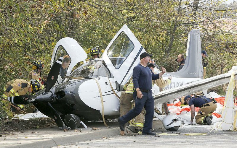 Emergency responders secure the scene of a small plane crash Tuesday on Martin Luther King Boulevard in Fayetteville. Former Wal-Mart CEO Bill Simon and two other men were on the plane, which deployed a parachute after developing engine problems. All three men and one person on the ground suffered nonlife-threatening injuries. More photos are available at arkansasonline.com/galleries.