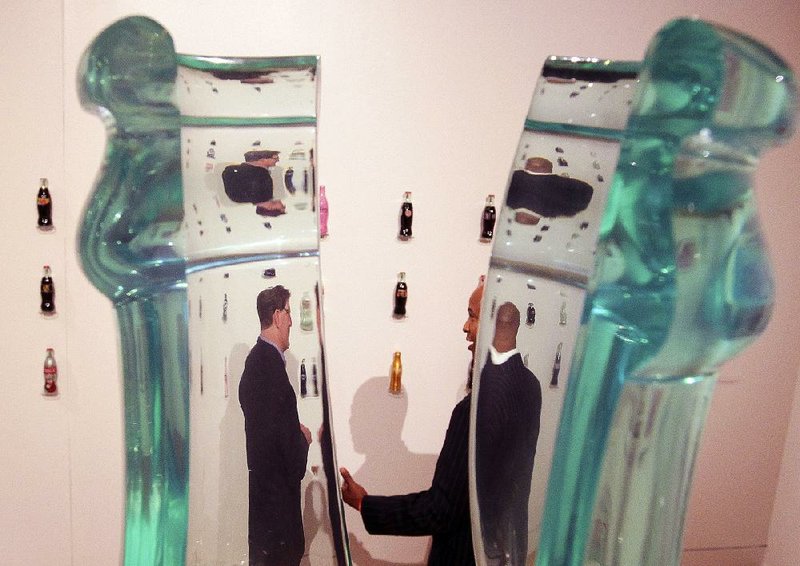Coca-Cola historian Ted Ryan (left) and Joe Gentry, Coca-Cola general manager of the Memphis and Little Rock market unit, are seen through the neck of a large bottle during a preview of the Clinton Presidential Center’s temporary exhibit, Coca-Cola: An American Original. 