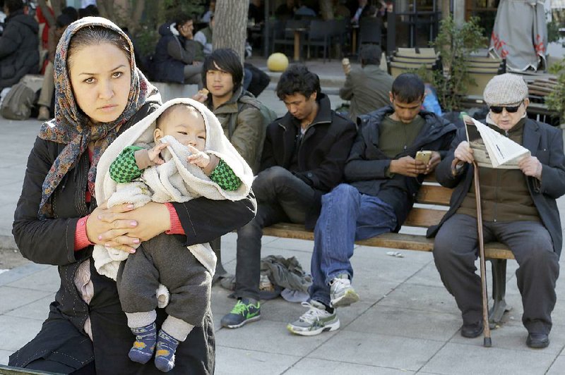 An Afghan woman and baby sit with other migrants and Greeks Tuesday at Victoria Square in Athens, where hundreds of migrants stay temporarily before continuing to more prosperous northern European countries. 