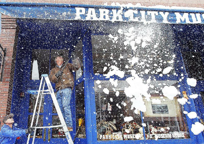 Park City, Utah, city worker Blair Smith clears off an awning Tuesday as wet, heavy snow falls in the area, closing schools and knocking out power.The system was moving east, carrying a slight threat of severe thunderstorms for Arkansas. 