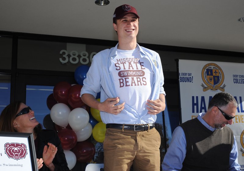 Antonio Thomas (center) of Haas Hall Academy, a swimmer for the Razorback Aquatic Club AquaHawgs swim team, shows off his Missouri State T-shirt Thursday after signing a letter of intent to swim for the Bears during a ceremony at the school. Beside him are his mother, Stephanie, and father, Aaron.